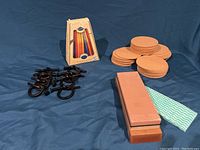 Lot items: cast iron napkin holders, cork coasters, wet stone sharpener, and Chanukah candles on blue surface