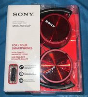 Front view of Sony MDR-ZX310AP headphones in original packaging showing red ear cups, Sony logo, and features like high-quality balanced sound, compatibility with smartphones, hands-free phone call, compact folding.