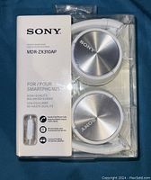 Front view of the Sony MDR-ZX310AP headphones in original plastic packaging with product information and logo visible