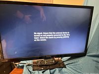 Panasonic 32 inch TV powered on showing 'No signal' message on screen with remote placed in front.