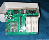 Top view of the Parallax Board of Education microcontroller development board showing integrated breadboard, labeled I/O pins, power jack, reset button, and other components.