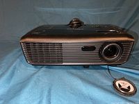 Front view of black Optoma projector showing lens, focus ring, and ventilation grill.