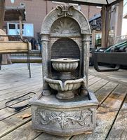 Full front view of small decorative water fountain showing arched back, two tier bowl spout and base basin with ornate front panel detail