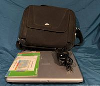 Closed Toshiba Satellite laptop with power cord, original Windows XP software, and black Samsonite laptop case laid on blue fabric.