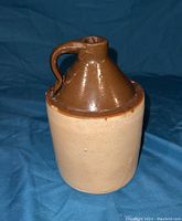 Front view of vintage whiskey jug showing brown glazed neck and handle with a light tan bottom.