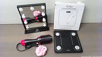 Overview of makeup mirror with LED bulbs, Bluetooth scale with sensors and box, multifunctional hair dryer with comb, and pink hair curler.