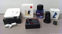 Overview of the entire lot showing all items including the wireless charging station, smartphone stand box, headphones, Bluetooth speaker, and charging dock with adapter.
