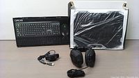 Wide view showing keyboard and mouse box, laptop cooling fan, wired headphones and power adapter on table.
