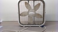 Front view of the white Lasko box fan showing metal grille and five blades.