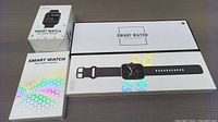 Four smart watch boxes showing product images and branding on white packaging with colorful geometric patterns.