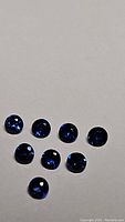 Eight natural royal blue round-cut sapphires on a neutral background showing their color and clarity.