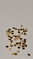 Close-up front view of multiple tiny round yellow sapphires, diamond cut, laid out on a white background, showing their color and sparkle.