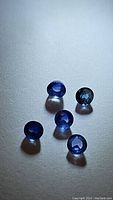 Five blue sapphire gemstones on a white background under neutral lighting showing mixed blue tones and round cabochon shapes.