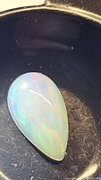 Pear-shaped Ethiopian opal cabochon showing play of color on black background.