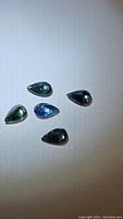 Five natural pear-shaped sapphires in a range of blue to green colors, arranged on a white surface.