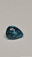 Close-up image of a pear cut deep lagoon blue Cambodian zircon gemstone showing clear facets and brilliance.