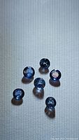 Six natural round cut blue sapphires placed on a neutral surface, showing top and side views with light reflections