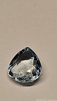 Clear close-up image of pear-shaped aquamarine showing its natural sky blue color and internal clarity features placed on a light background.