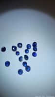 Photo showing a scattered group of small round blue sapphires under a light spot on white background, highlighting their deep blue color and round shape.
