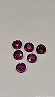 Six round faceted natural rubies with deep hot purple pink red color on a neutral background