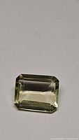 Close-up photo of natural lemon citrine gemstone with emerald cut showing the rectangular faceted shape and pale yellow colour.