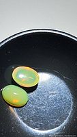 Close-up photo of two oval cabochon cut natural Ethiopian opals showing orange-red flashes against a dark surface.