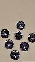Close-up photo of seven round cut natural tanzanite gemstones with blue to purple color on a neutral background.