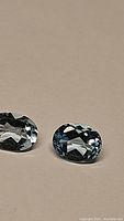 Pair of oval natural lagoon blue topaz gemstones on neutral background showing facets and color.