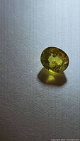 Close-up photo of natural yellow sapphire gemstone showing oval cut and bright canary yellow color on gray textured surface.