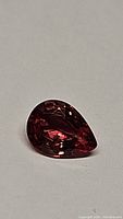 Pear-shaped padparadscha sapphire displaying pinkish-orange with blue streaks, detailed facet cut visible, on a light background.