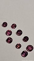 Ten round faceted pink to purple sapphires arranged on a flat surface showing their color and size range.