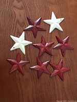 Photo showing six red and two white metal stars arranged on wooden surface, each star approximately 3 inches diameter.
