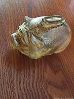 Angled top view of vintage glass piggy bank showing textured glass surface with golden tint, coin slot on top, and overall aged condition.