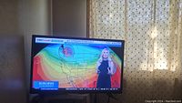 TV switched on showing weather forecast news program, mounted in living room environment.