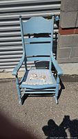 Antique wooden rocker chair with blue paint and striped floral seat pad, shown outdoors.