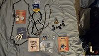 Full overview of various necklaces, earrings, jewelry pieces, and bags containing small jewelry parts on a gray fabric surface.