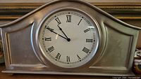 Front view of a traditional shape mantle clock with silver or brushed nickel finish and Roman numeral dial.