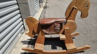 Side angle showing the solid wood construction with attached dark brown leather saddle embroidered with 'Tony the Pony'. Visible grain and solid rocker base.