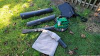 Full set of blower and mulching vac items including the main unit, fabric bag, three different nozzles, carrying bag, and small gas can, laid out on grass near a fence.