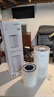 Photo showing the Cuckoo air purifier, unopened extra filter, and original box on table in basement setting.
