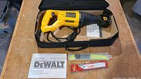 DeWalt DW304P reciprocating saw in black soft case with instruction manual and assorted blades, all displayed on wooden surface.