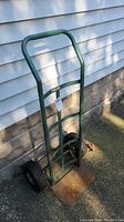 Metal dolly standing upright against house siding, visible handle, tires, and rusty base plate.