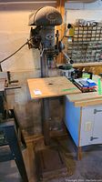 Full view of the Beaver Tools drill press showing the full height with a wooden work table and metal base.