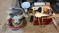Overview of multiple electrical cables, coils of wire, power bars, and cords arranged around and inside red plastic crate.