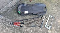 Top view of floor creeper alongside bolt cutters, three crowbars, hammer, and hacksaw on ground.