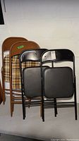 Photo showing two plaid fabric folding chairs beside two black padded folding chairs all folded up.