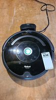 Top view of black iRobot Roomba vacuum and charger base on wooden surface with visible wear and scratches.