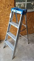 Front-side view of the 48 inch Caradon Lite aluminum step ladder showing three wide steps and blue plastic top tray with paint stains.