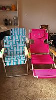 Two folding chairs, one with blue and white woven strap design and the other a pink lawn lounger with cup holder and padded face opening.