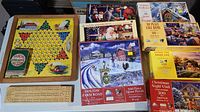 Photo showing Chinese checkers board with marbles, cribbage board, and several boxed jigsaw puzzles including Holiday Farm Road and Holiday Birdhouse.